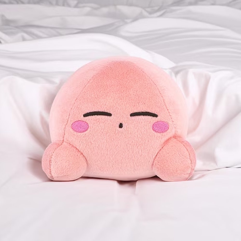 An officially licensed soft, round pink Kirby plush cushion resting peacefully with embroidered closed eyes and rosy cheeks