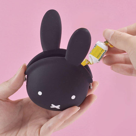  A close-up photograph of a woman's hand holding a small, jet black Miffy character pouch made of soft, flexible premium silicone. Part of the Official Miffy Mini Pochibi series, aesthetic alternative; a durable, tactile, and minimalist Zen bunny purse designed for adult mental wellness and nostalgic daily organization.