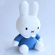 Official Miffy sitting plush wearing a classic blue dress. This pure white minimalist doll is designed for adult collectors seeking childhood nostalgia and visual rest. Its stable sitting posture makes it a perfect soothing desktop companion or a nostalgic shelf decor piece for a high-stress modern lifestyle