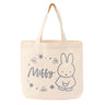 An officially licensed Miffy canvas tote bag in a cream color, surrounded by flowers with the name "Miffy" in a grey script font.