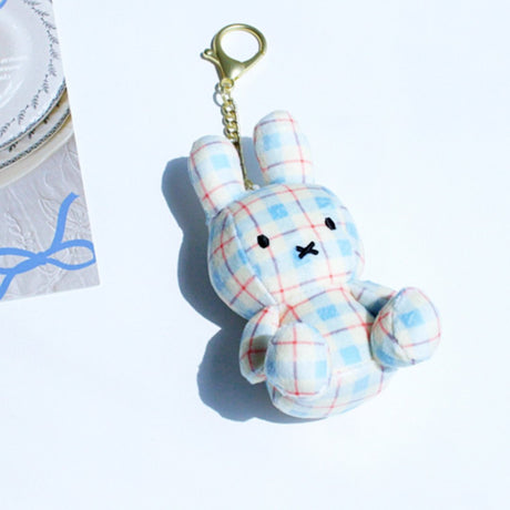 Officially licensed Miffy plush keychain featuring a blue and white plaid/checkered fabric pattern. The soft plush toy is shaped like Miffy, with black embroidered eyes and an 'X' mouth, and includes a gold-tone clasp for use as a bag charm or collector's item.