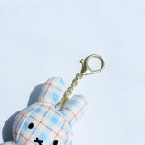 Officially licensed Miffy plush keychain featuring a blue and white plaid/checkered fabric pattern. The soft plush toy is shaped like Miffy, with black embroidered eyes and an 'X' mouth, and includes a gold-tone clasp for use as a bag charm or collector's item.