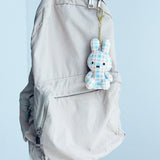 Officially licensed Miffy plush keychain featuring a blue and white plaid/checkered fabric pattern. he soft plush toy keychain attached to a gray backpack against a light blue background