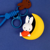 A collection of Miffy dream figure keychains in various poses, including Miffy reading a book, sleeping on a moon, and holding a yellow star, shown with green and blue accessories.