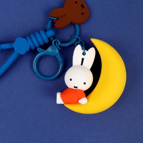 A collection of Miffy dream figure keychains in various poses, including Miffy reading a book, sleeping on a moon, and holding a yellow star, shown with green and blue accessories.