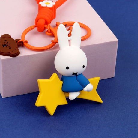 A collection of Miffy dream figure keychains in various poses, including Miffy reading a book, sleeping on a moon, and holding a yellow star, shown with green and blue accessories.