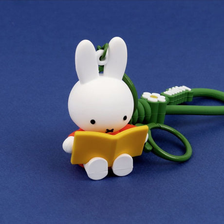 A collection of Miffy dream figure keychains in various poses, including Miffy reading a book, sleeping on a moon, and holding a yellow star, shown with green and blue accessories.
