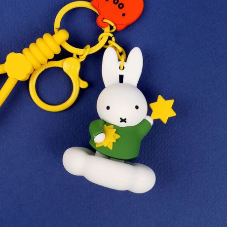 A collection of Miffy dream figure keychains in various poses, including Miffy reading a book, sleeping on a moon, and holding a yellow star, shown with green and blue accessories.