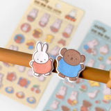 Two officially licensed Miffy Fuzzy Cushion Sticker sheets in cream and mint colors, showcased alongside a decorated phone case and earbud case. The sticker sheets are filled with small, textured, raised stickers depicting Miffy the bunny and her friends engaging in daily activities like baking and gardening.
