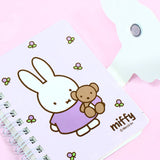 A series of officially licensed Miffy spiral notebooks in pastel pink, blue, and purple, featuring a large magnetic character buckle. The interior shows lined paper with a small Miffy graphic in the bottom corner, highlighting the notebook's functional and cute design.