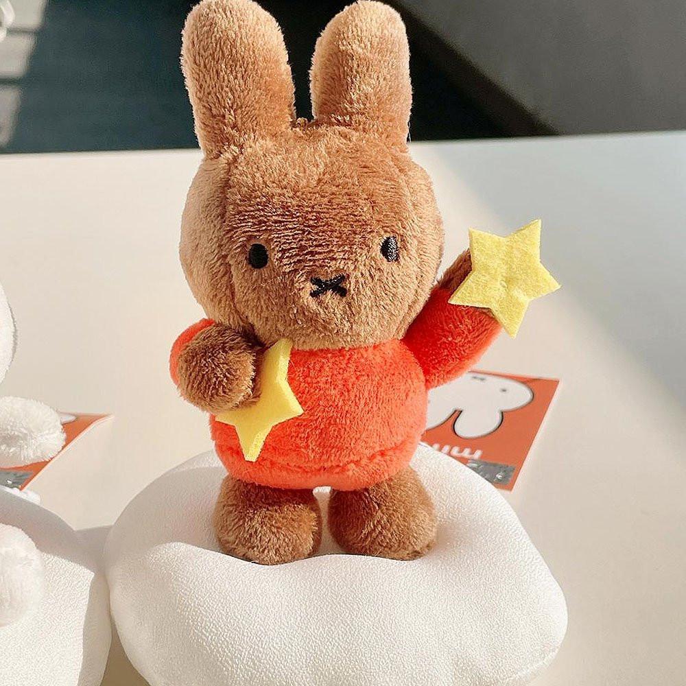 Official Miffy Melanie Dream Mascot Plush Keychain holding yellow stars; a brown Melanie rabbit plush in an orange sweater, designed as a premium nostalgic bag charm and minimalist Zen accessory for adult mental wellness and office-core decor.