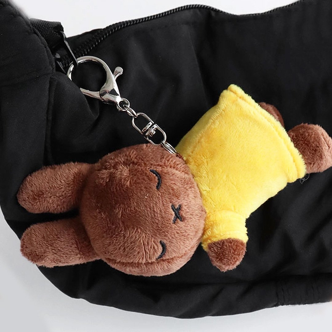Officially licensed Miffy sleeping plush keychain featuring embroidered closed eyes and an 'X' mouth. Brown Miffy plush wearing yellow top. The soft plush toy keychain attached to a black  backpack .