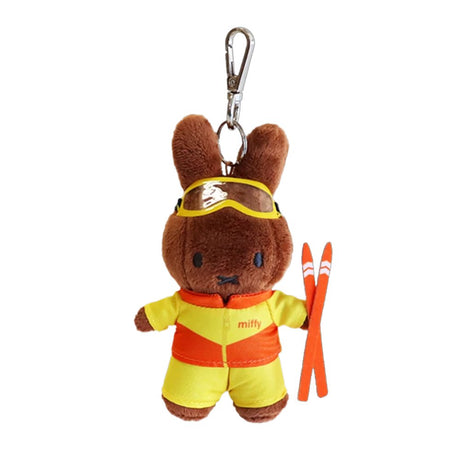 A chocolate-brown, officially licensed Miffy's Melanie plush keychain wearing a bright yellow and orange ski jump suit and goggles. The bunny holds miniature orange skis and is attached to a silver metal clip, ready for winter sports adventures.
