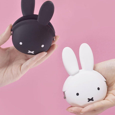  A close-up photograph of a woman's hand holding a small, matte white Miffy character pouch made of soft, flexible premium silicone. Part of the Official Miffy Mini Pochibi series, which includes a jet-black aesthetic alternative; a durable, tactile, and minimalist Zen bunny purse designed for adult mental wellness and nostalgic daily organization.