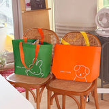 Green and orange Tarpaulin tote bags with miffy and Snuffy designs on chairs in a room.