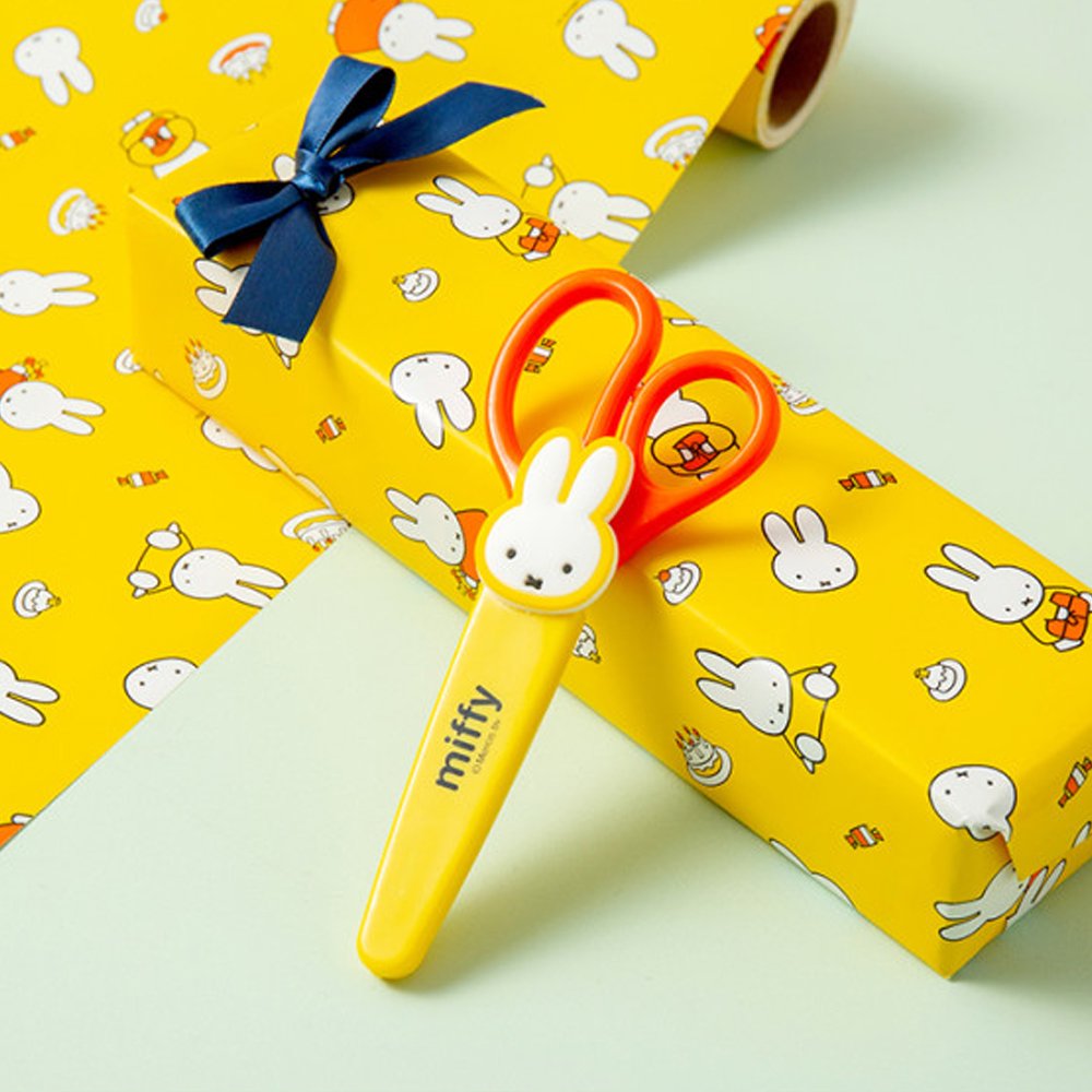 An officially licensed pair of Miffy safety scissors packaged on a colorful backing card, featuring bright orange handles and a protective yellow cap adorned with a die-cut Miffy bunny head.
