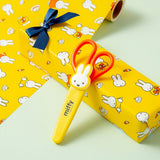 An officially licensed pair of Miffy safety scissors packaged on a colorful backing card, featuring bright orange handles and a protective yellow cap adorned with a die-cut Miffy bunny head.
