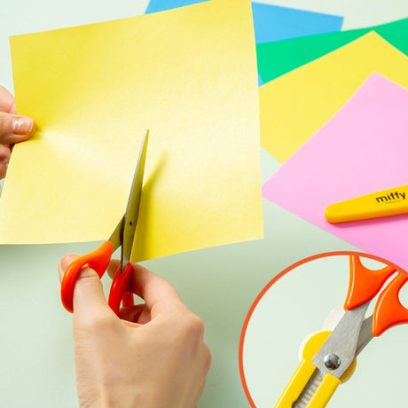 An officially licensed pair of Miffy safety scissors packaged on a colorful backing card, featuring bright orange handles and a protective yellow cap adorned with a die-cut Miffy bunny head.
