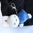 Officially licensed Miffy sleeping plush keychain featuring embroidered closed eyes and an 'X' mouth. Miffy plush wearing green top. The soft plush toy keychain attached to a black  backpack .