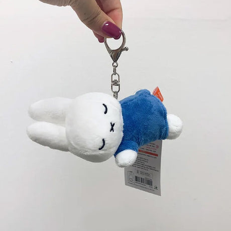 Officially licensed Miffy sleeping plush keychain featuring embroidered closed eyes and an 'X' mouth. Miffy plush wearing blue top. Ideal collectible bag charms, backpack zipper pulls or gift.