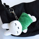 Officially licensed Miffy sleeping plush keychain featuring embroidered closed eyes and an 'X' mouth. Miffy plush wearing green top. The soft plush toy keychain attached to a black  backpack .