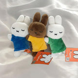 Set of three officially licensed Miffy plush sleeping keychains. The soft dolls include two white Miffy plush (wearing green and blue top ) and one brown Miffy plush(wearing a yellow top), all with embroidered closed eyes and an 'X' mouth. Ideal collectible bag charms or backpack zipper pulls.