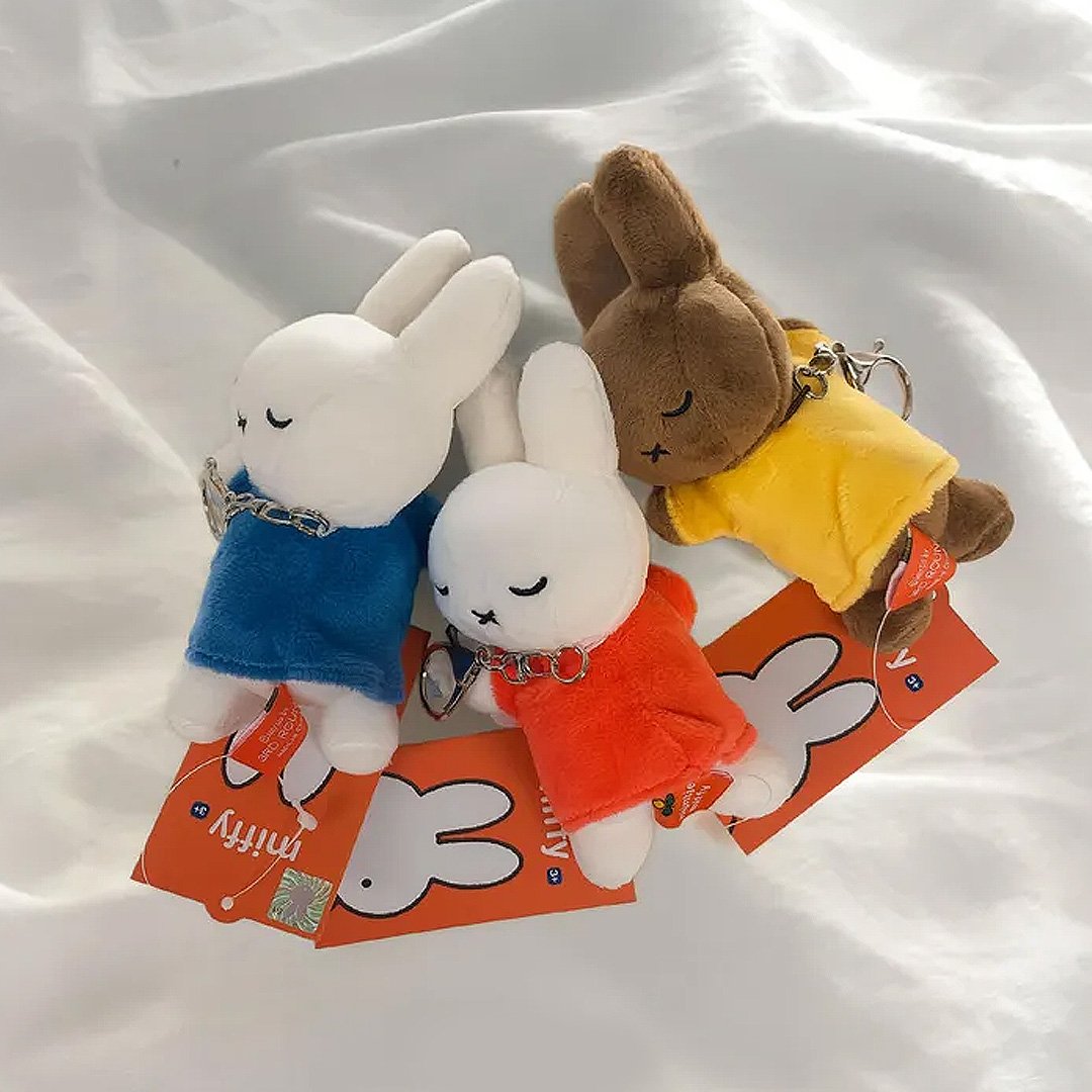 Set of three officially licensed Miffy plush sleeping keychains. The soft dolls include two white Miffy plush (wearing red and blue top ) and one brown Miffy plush(wearing a yellow top), all with embroidered closed eyes and an 'X' mouth. Ideal collectible bag charms or backpack zipper pulls.