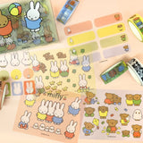 An officially licensed Miffy stationery set featuring five rolls of decorative washi tape and five shiny sticker sheets displayed with a transparent storage case. The collection showcases classic Dick Bruna illustrations of Miffy the rabbit and friends in soft pastel colors.
