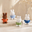 Four officially licensed Miffy plush keychains wearing knit sweaters in orange, green, light blue, and dark blue standing together. Each plush includes an attached silver chain with a lobster clasp at the top.
