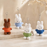 Four officially licensed Miffy plush keychains wearing knit sweaters in orange, green, light blue, and dark blue standing together. Each plush includes an attached silver chain with a lobster clasp at the top.