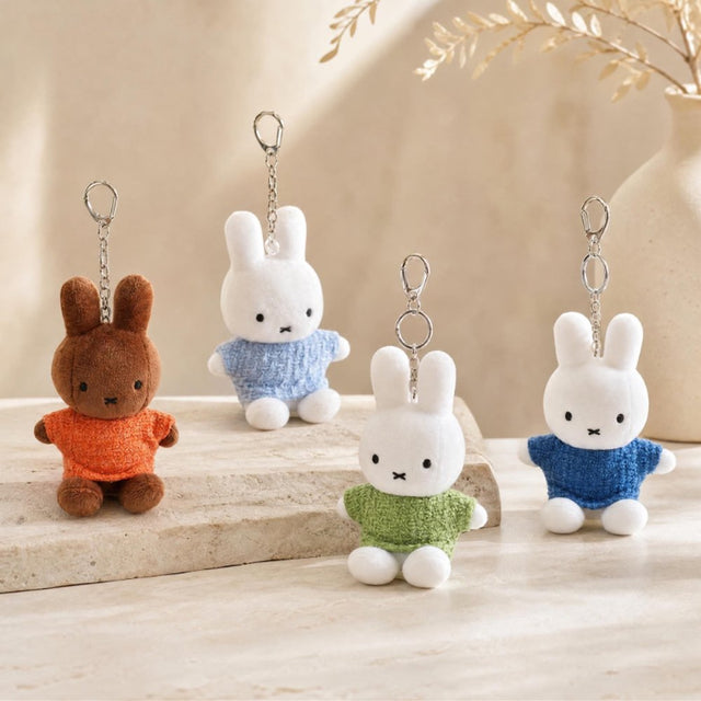 Four officially licensed Miffy plush keychains wearing knit sweaters in orange, green, light blue, and dark blue standing together. Each plush includes an attached silver chain with a lobster clasp at the top.