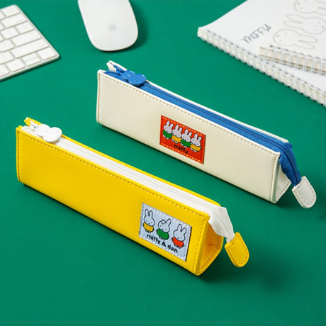 Two officially licensed slim, triangular Miffy pencil cases, featuring one in bright yellow with a white zipper and a "miffy & dan" patch, and the other in cream-colored with a bold blue zipper and a red "miffy" patch.
