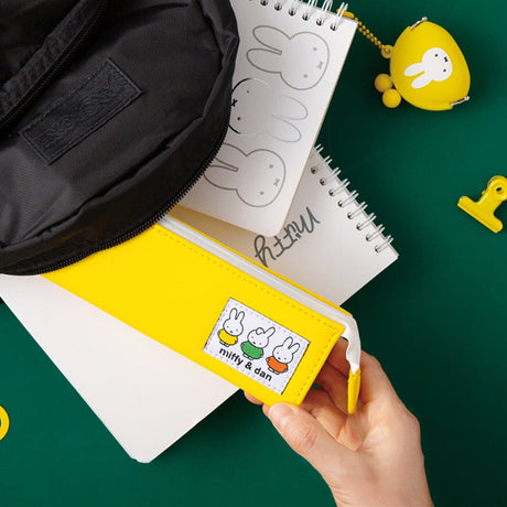 Two officially licensed slim, triangular Miffy pencil cases, featuring one in bright yellow with a white zipper and a "miffy & dan" patch, and the other in cream-colored with a bold blue zipper and a red "miffy" patch.
