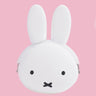  A close-up photograph of a woman's hand holding a small, matte white Miffy character pouch made of soft, flexible premium silicone. Part of the Official Miffy Mini Pochibi series, which includes a jet-black aesthetic alternative; a durable, tactile, and minimalist Zen bunny purse designed for adult mental wellness and nostalgic daily organization.