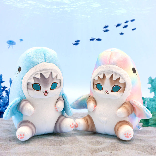 Two officially licensed Mofusand "Shark Meow" plush toys: a brown tabby cat in a rainbow pastel shark hoodie and a grey tabby cat with a playful open-mouth expression in a light blue shark hoodie, both featuring deep blue eyes and pink embroidered paw pads.