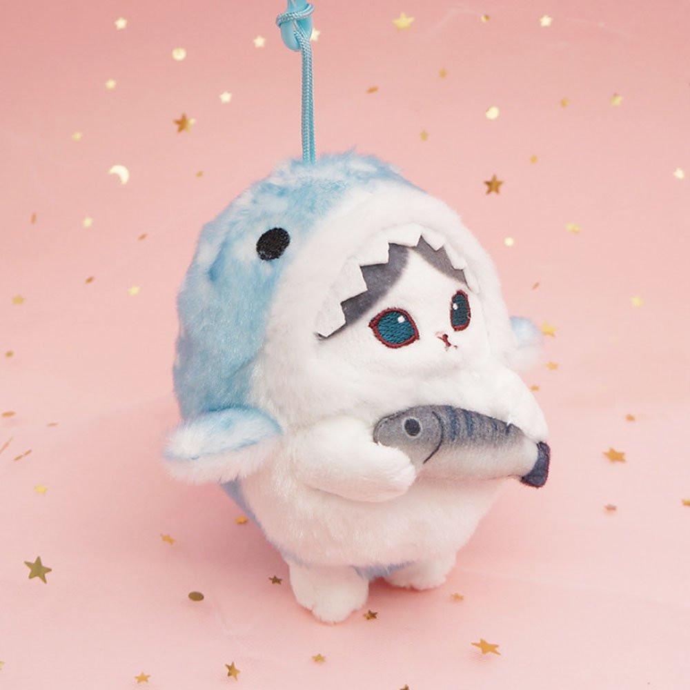 An officially licensed Mofusand shark cat plush keychain featuring a fluffy blue tabby kitten wearing a blue shark onesie with embroidered details