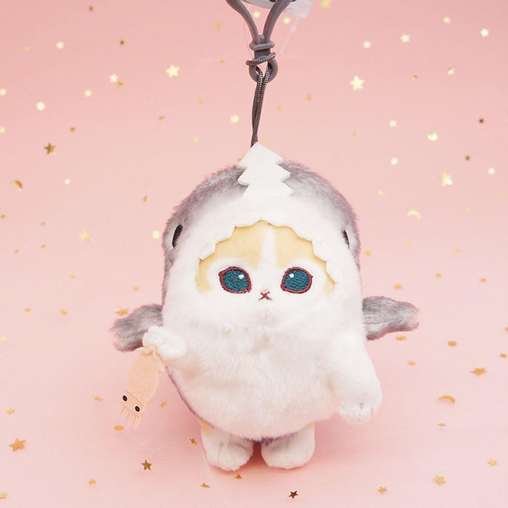 An officially licensed Mofusand shark cat plush keychain featuring a fluffy cream tabby kitten wearing a gray shark onesie with embroidered details