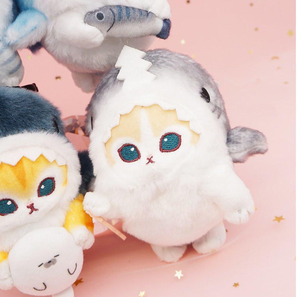 An officially licensed Mofusand shark cat plush keychain featuring a fluffy cream tabby kitten wearing a gray shark onesie with embroidered details