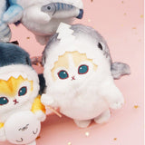 An officially licensed Mofusand shark cat plush keychain featuring a fluffy cream tabby kitten wearing a gray shark onesie with embroidered details