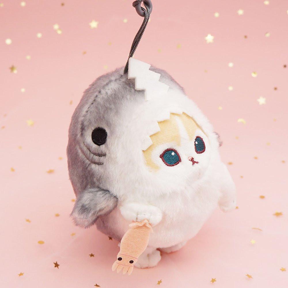 An officially licensed Mofusand shark cat plush keychain featuring a fluffy cream tabby kitten wearing a gray shark onesie with embroidered details