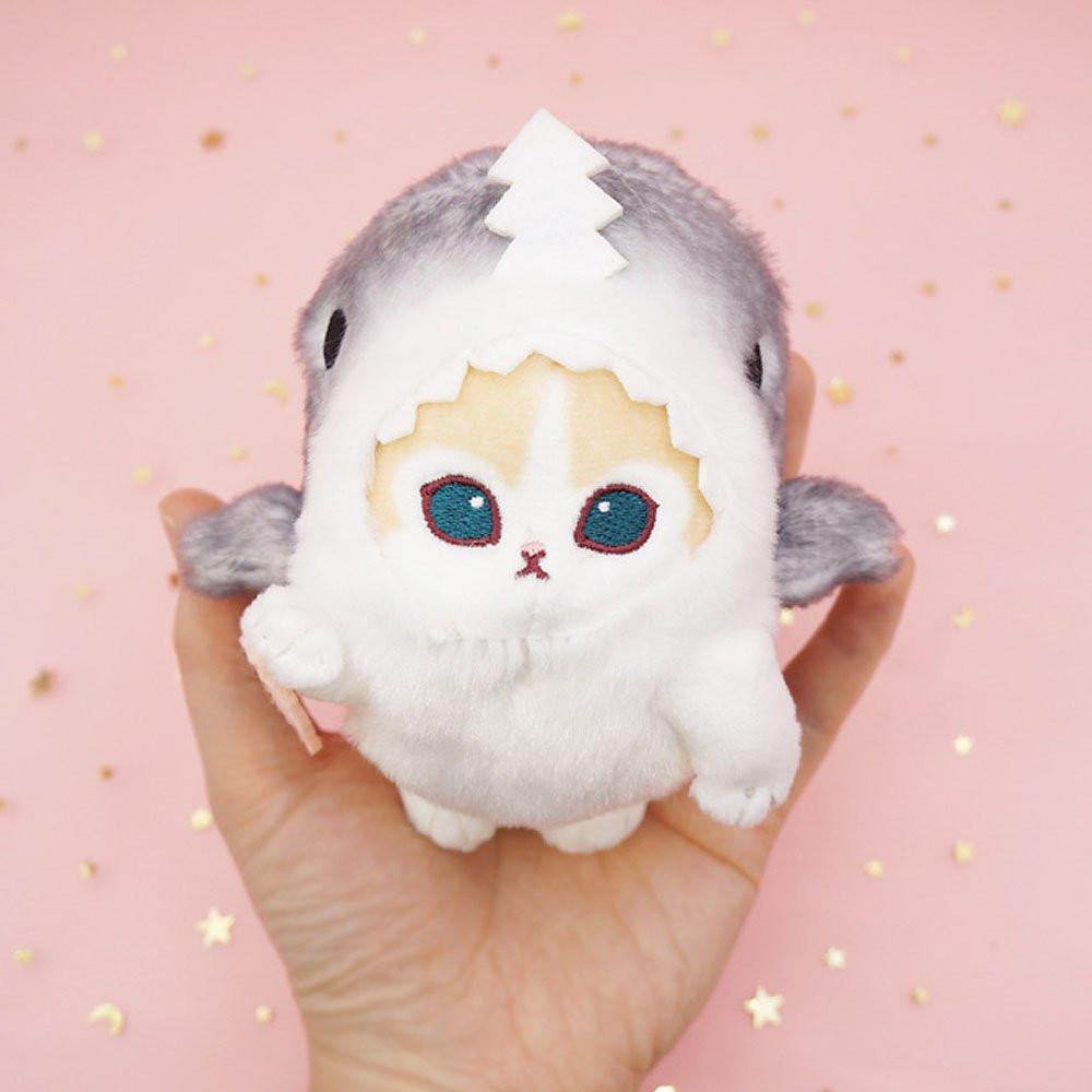 An officially licensed Mofusand shark cat plush keychain featuring a fluffy cream tabby kitten wearing a gray shark onesie with embroidered details