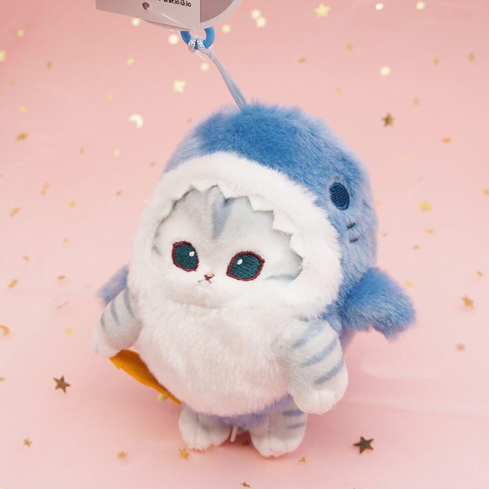 An officially licensed Mofusand shark cat plush keychain featuring a fluffy gray tabby kitten wearing a blue shark onesie with embroidered details
