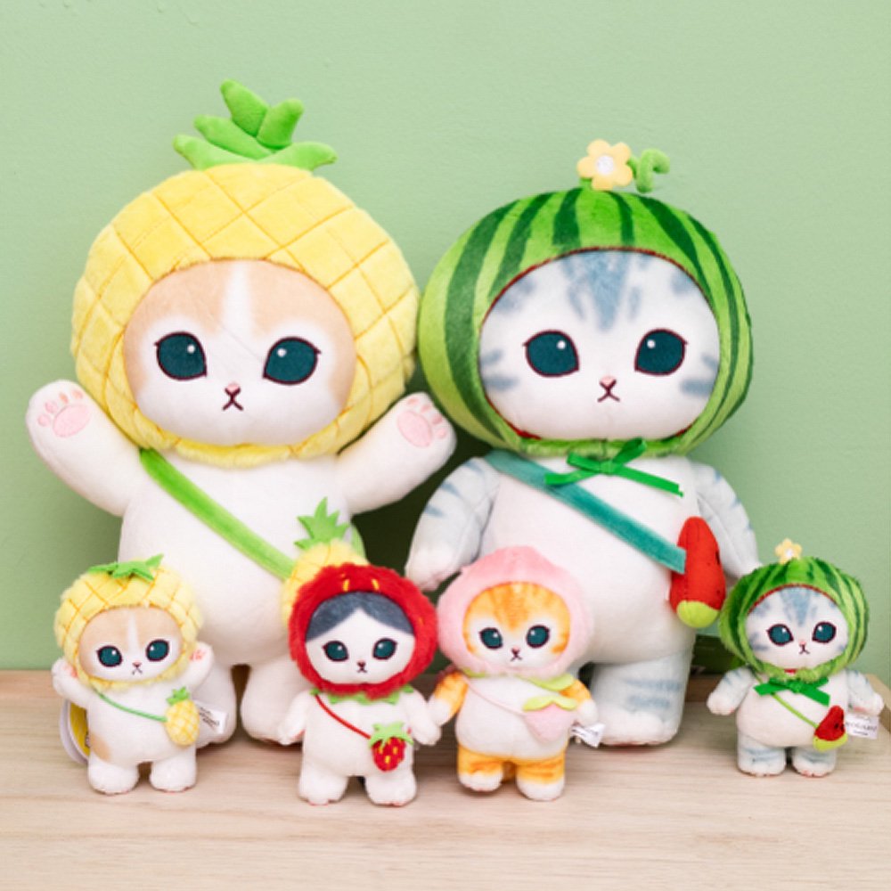 Four officially licensed Mofusand plush cat keychains wearing fruit-themed hoods: red strawberry hood, watermelon hood, pineapple hood, and pink peach hood. Each cat has a matching fruit-shaped crossbody bag and a colored plastic clip.