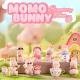 A group of officially licensed Momo Bunny Strawberry Town figures displayed in a miniature outdoor garden setting. The pink bunnies are dressed in various cute outfits, including a snowman suit, a pilot cap, and one sitting inside a strawberry-patterned teacup.