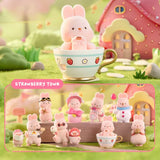 A group of officially licensed Momo Bunny Strawberry Town figures displayed in a miniature outdoor garden setting. The pink bunnies are dressed in various cute outfits, including a snowman suit, a pilot cap, and one sitting inside a strawberry-patterned teacup.