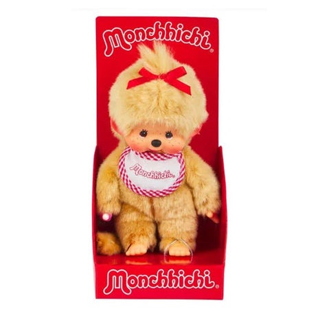 Officially licensed Monchhichi girl plush doll featuring unique golden-beige fur, a long tail, and a cute vinyl face with freckles. The doll has a bright red ribbon tied on its head and wears a white bib with a pink-and-white checkered border that reads "Monchhichi".
