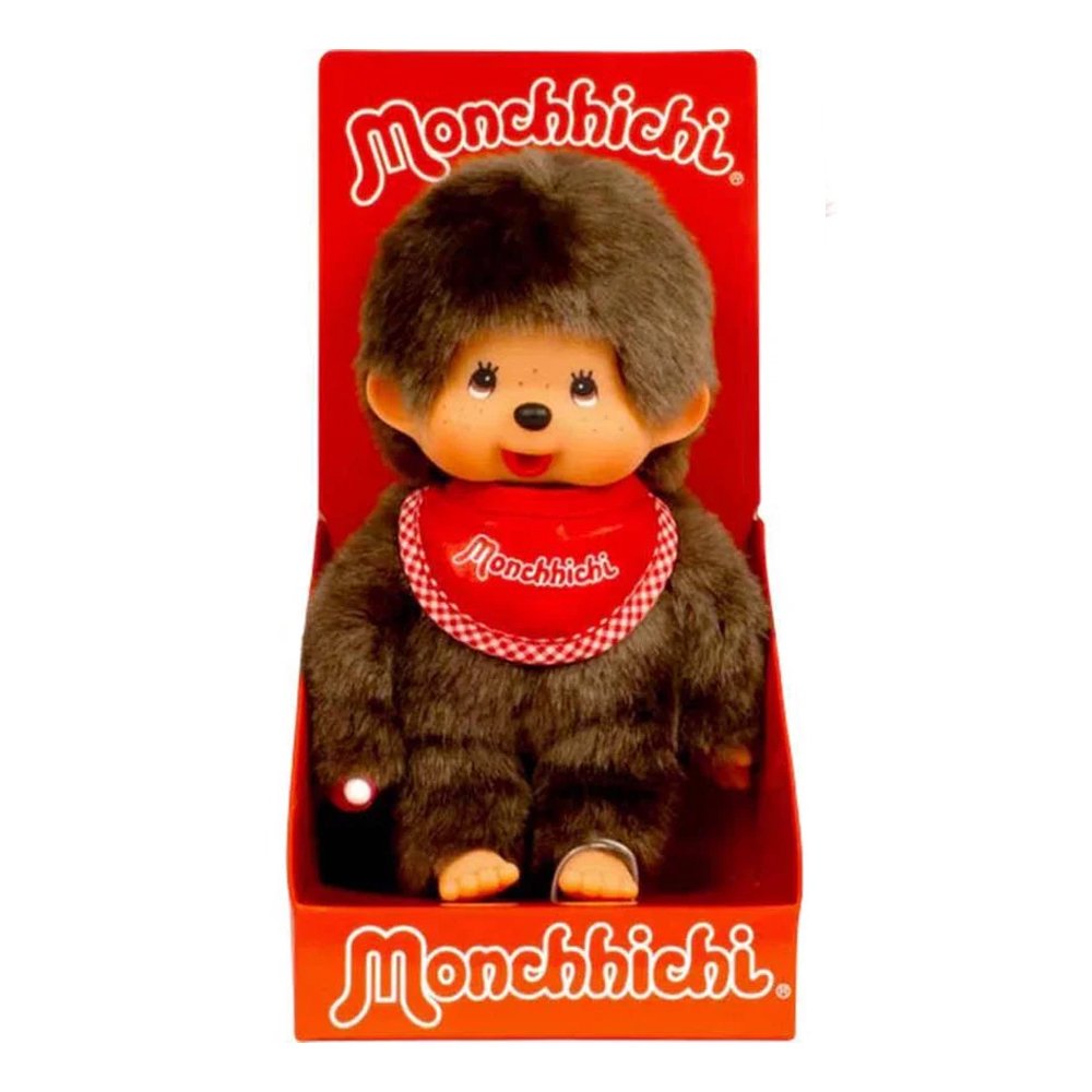 Officially licensed Monchhichi boy plush doll with soft brown fur, a long tail, and an adorable vinyl face with freckles. The doll is wearing a red bib with a checkered border and white text reading "Monchhichi" while holding its hand up to its mouth in its iconic thumb-sucking pose.
