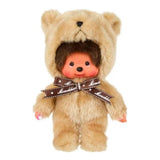 Officially licensed Monchhichi plush doll wearing a fuzzy, light beige teddy bear costume with a hood. The doll features a detailed vinyl face with rosy cheeks and is adorned with a brown ribbon tied around its neck reading "Monchhichi" in white text.
