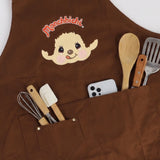 An officially licensed brown Monchhichi apron with red adjustable snap-button neck straps and front utility pockets