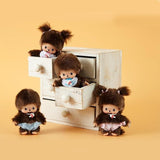 Four small baby Mochhichi dolls with brown hair and outfits in front of a wooden drawer on a yellow background